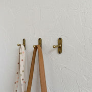 Solid brass wall hook with rounded ball end mounted on a textured white wall.