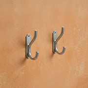 Chrome double wall hook mounted on a textured wall for towel and coat storage.