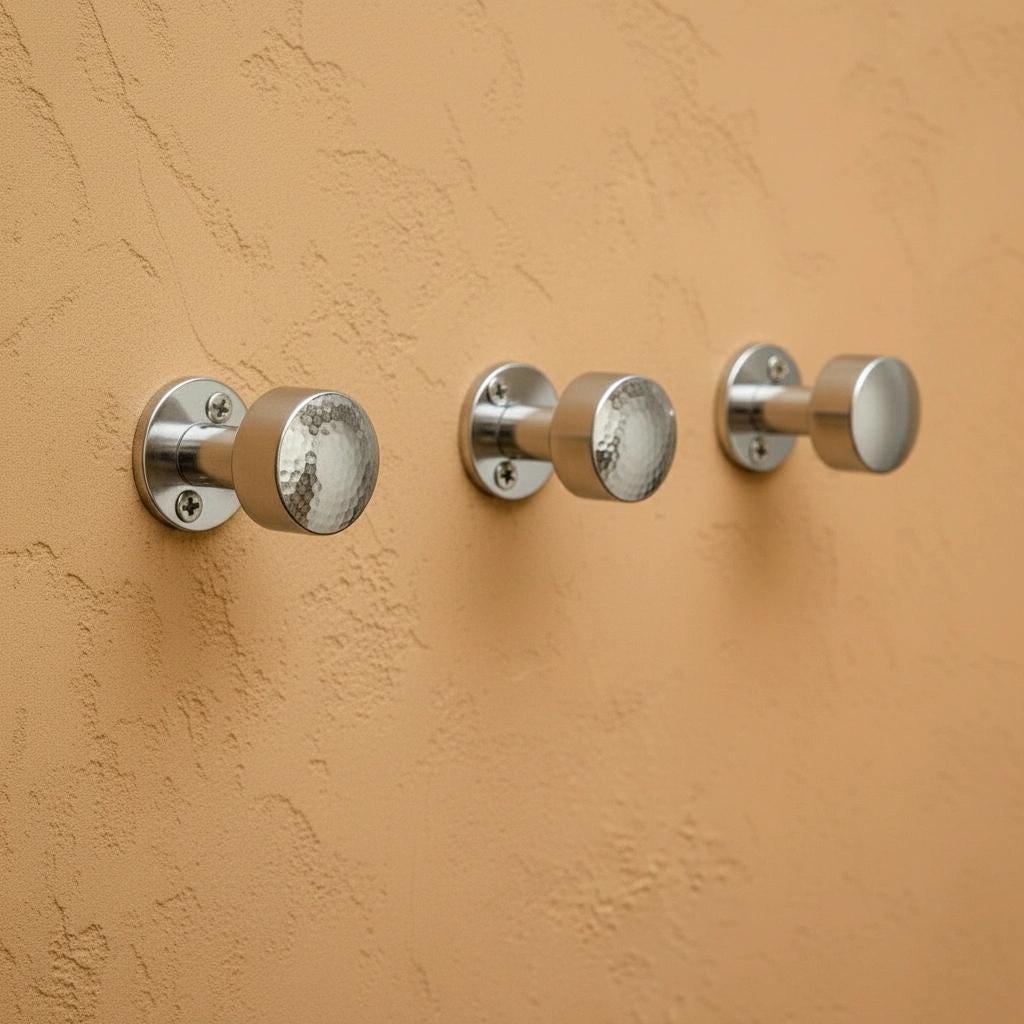 Hammered chrome wall hook mounted on textured wall, modern bathroom hardware for hanging towels and robes.