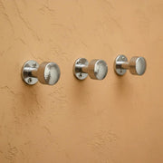 Hammered chrome wall hook mounted on textured wall, modern bathroom hardware for hanging towels and robes.