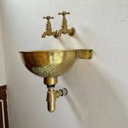 Handmade hammered brass wall-mounted sink with exposed brass drain and rustic vintage finish.