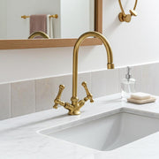 Solid brass bridge bathroom faucet with high arc spout installed on a marble vanity.