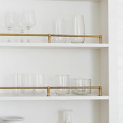 Single unlacquered brass shelf rail installed on a white open kitchen shelf.
