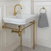 Unlacquered brass console sink stand legs supporting a wall-mounted bathroom sink.