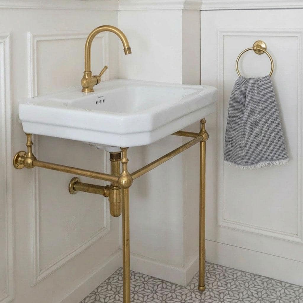 Unlacquered brass console sink stand legs supporting a wall-mounted bathroom sink.