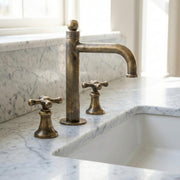 Aged brass widespread bathroom faucet with cross handles on marble vanity