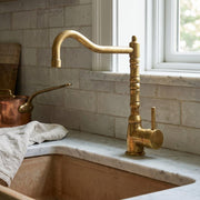 Unlacquered brass single handle kitchen faucet with sculpted decorative column.