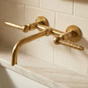 Handmade unlacquered brass wall mount bathroom faucet with hammered lever handles.
