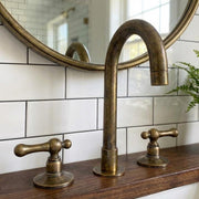 Handmade antique brass widespread bathroom faucet with high gooseneck spout and lever handles.
