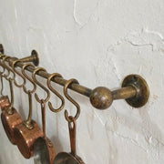 Wall mounted brass pot rail with hanging hooks displaying copper cookware.