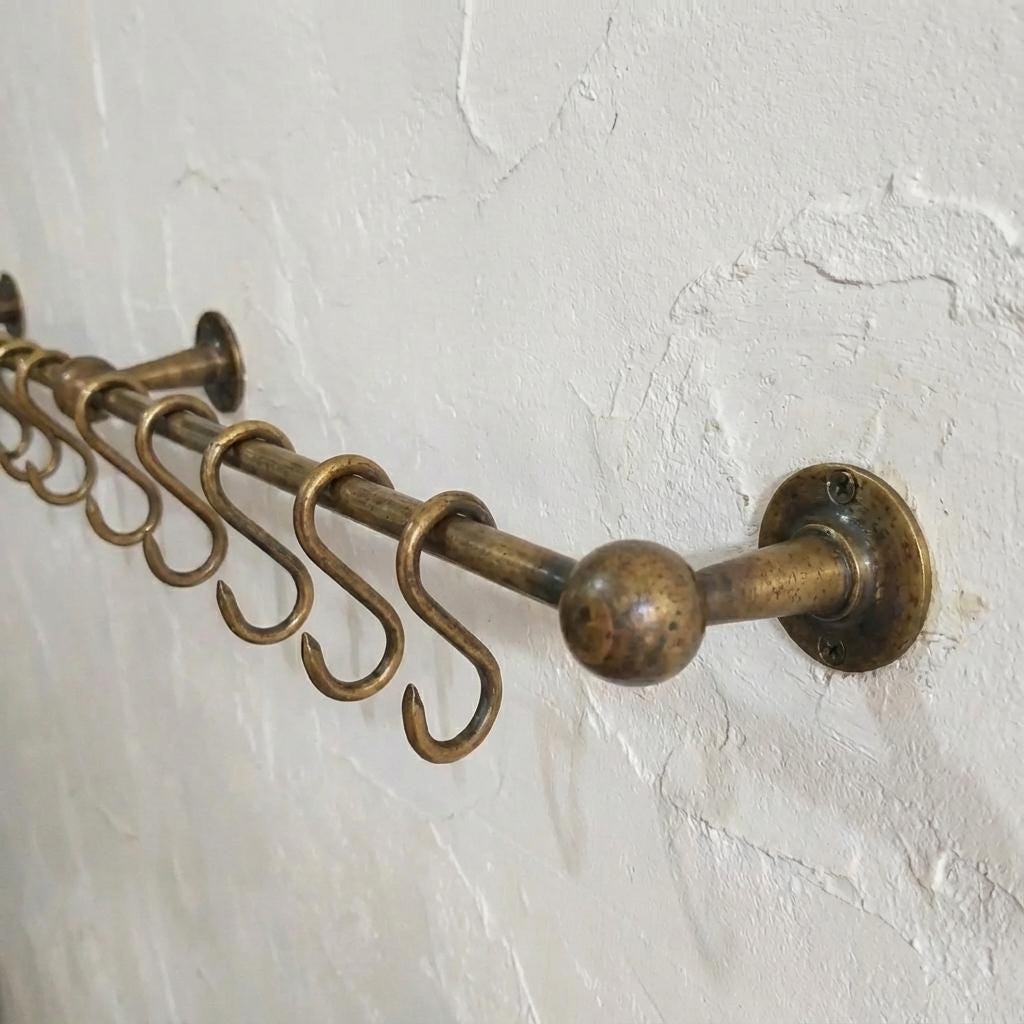 Decorative brass cookware rail with ball finials and hanging storage hooks.