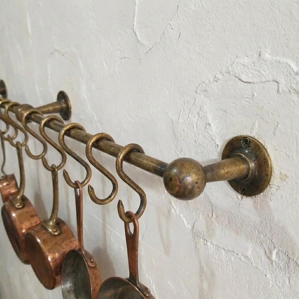 Traditional brass hanging rack installed on a textured plaster kitchen wall.