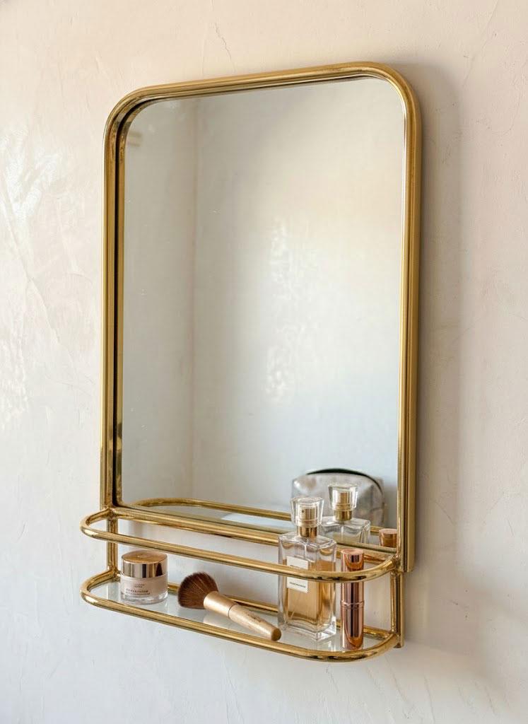 Arched brass vanity mirror featuring open shelf storage for bathroom accessories and cosmetics.