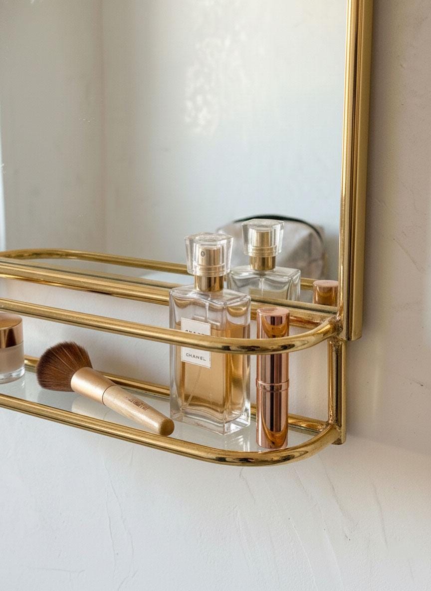 Traditional unlacquered brass bathroom mirror with storage rail above marble countertop.