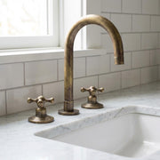 Antique brass bridge kitchen faucet with high-arc gooseneck spout and cross handles installed on a white marble countertop.