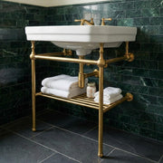 Solid brass console sink stand with integrated towel shelf installed beneath a wall-mounted bathroom sink.