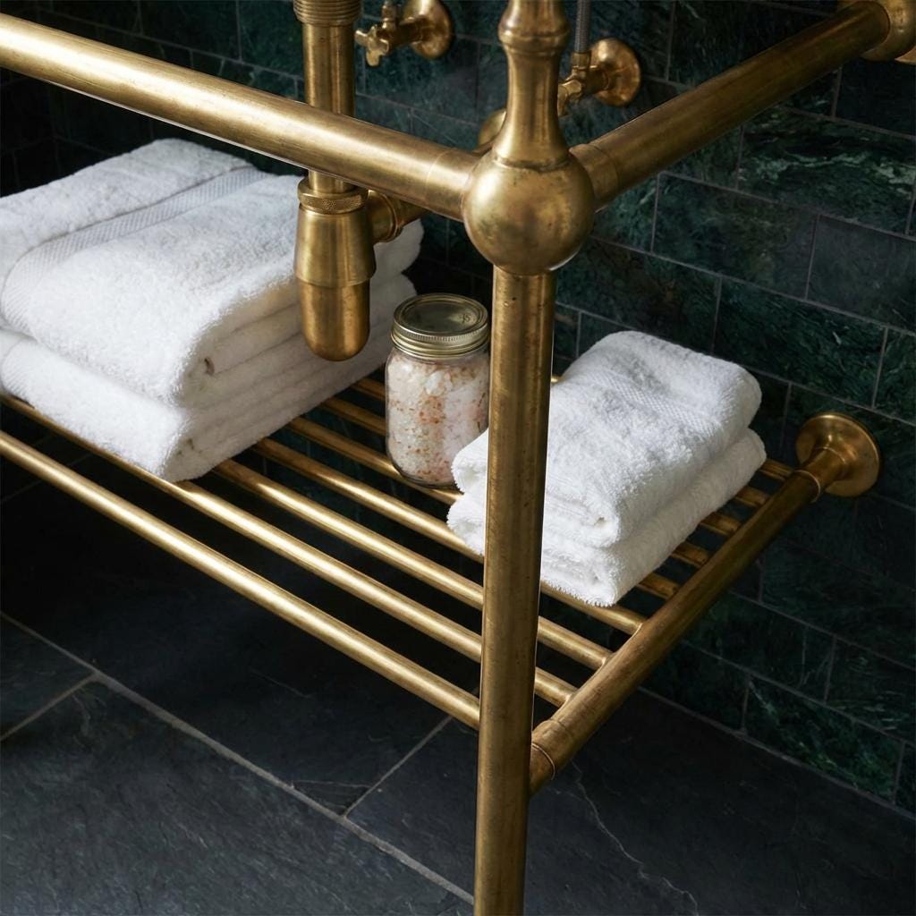 Unlacquered brass console vanity stand with integrated storage shelf, designed for wall-mounted bathroom sinks and towels.