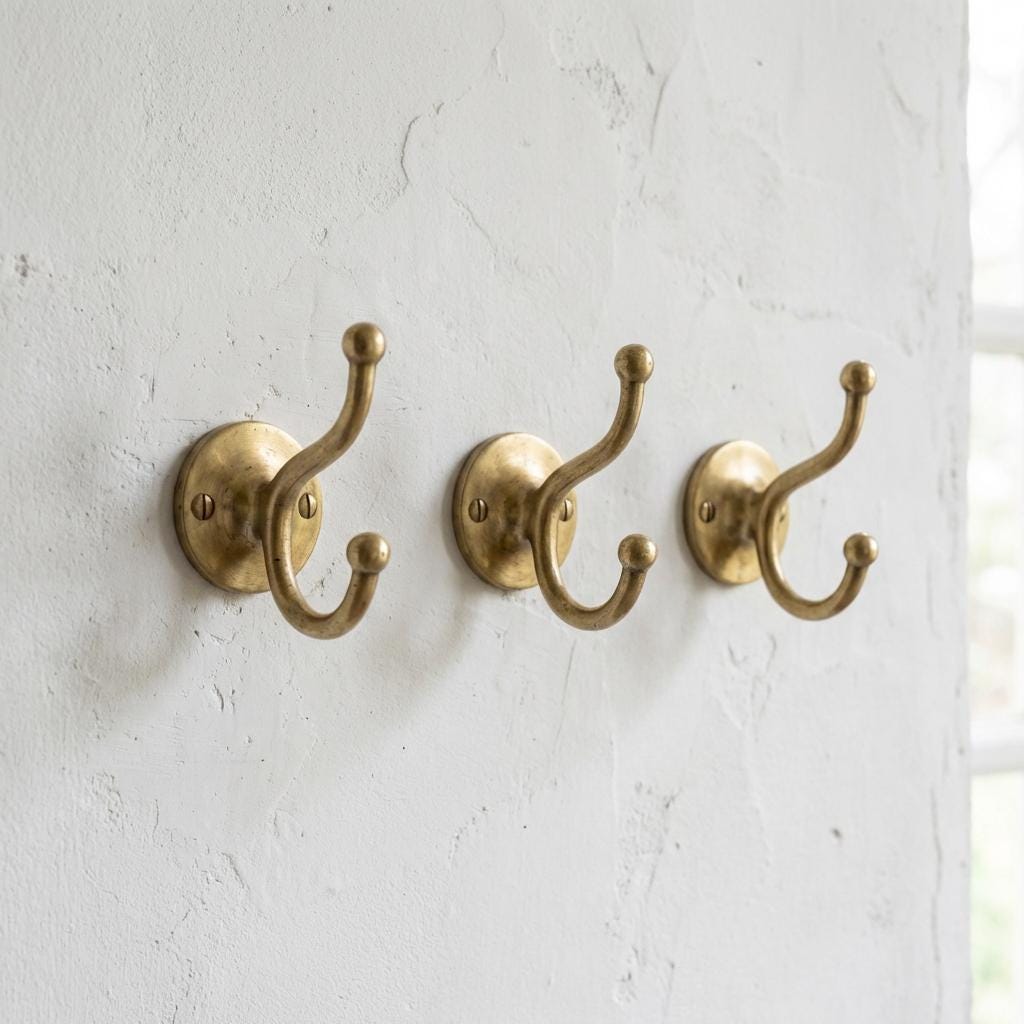 Solid brass double coat hook with round backplate for towels, robes, and bags.