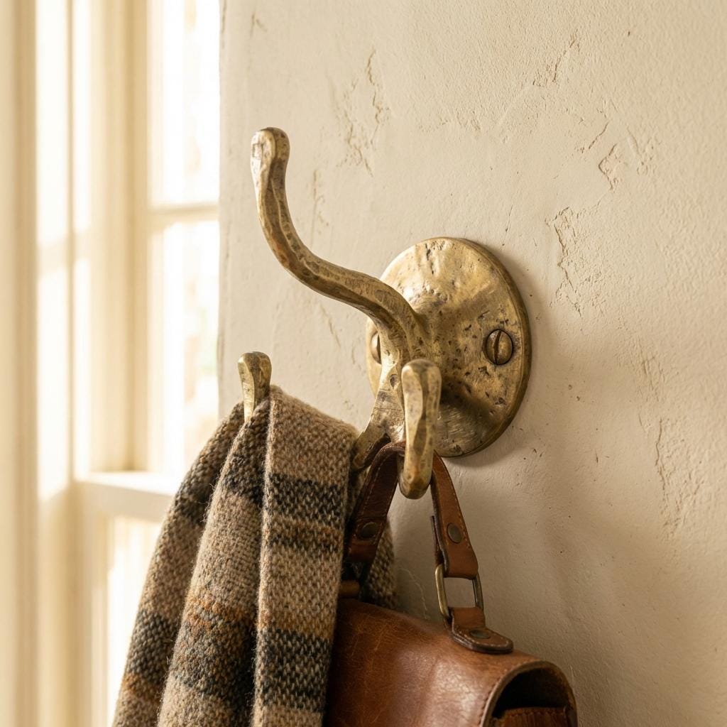 Hand forged brass triple wall hook mounted on a textured wall holding a scarf and leather bag.