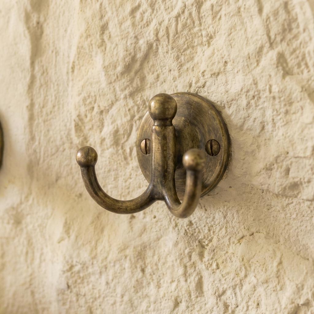 Solid brass double coat hook with round backplate for towels, robes, and bags.