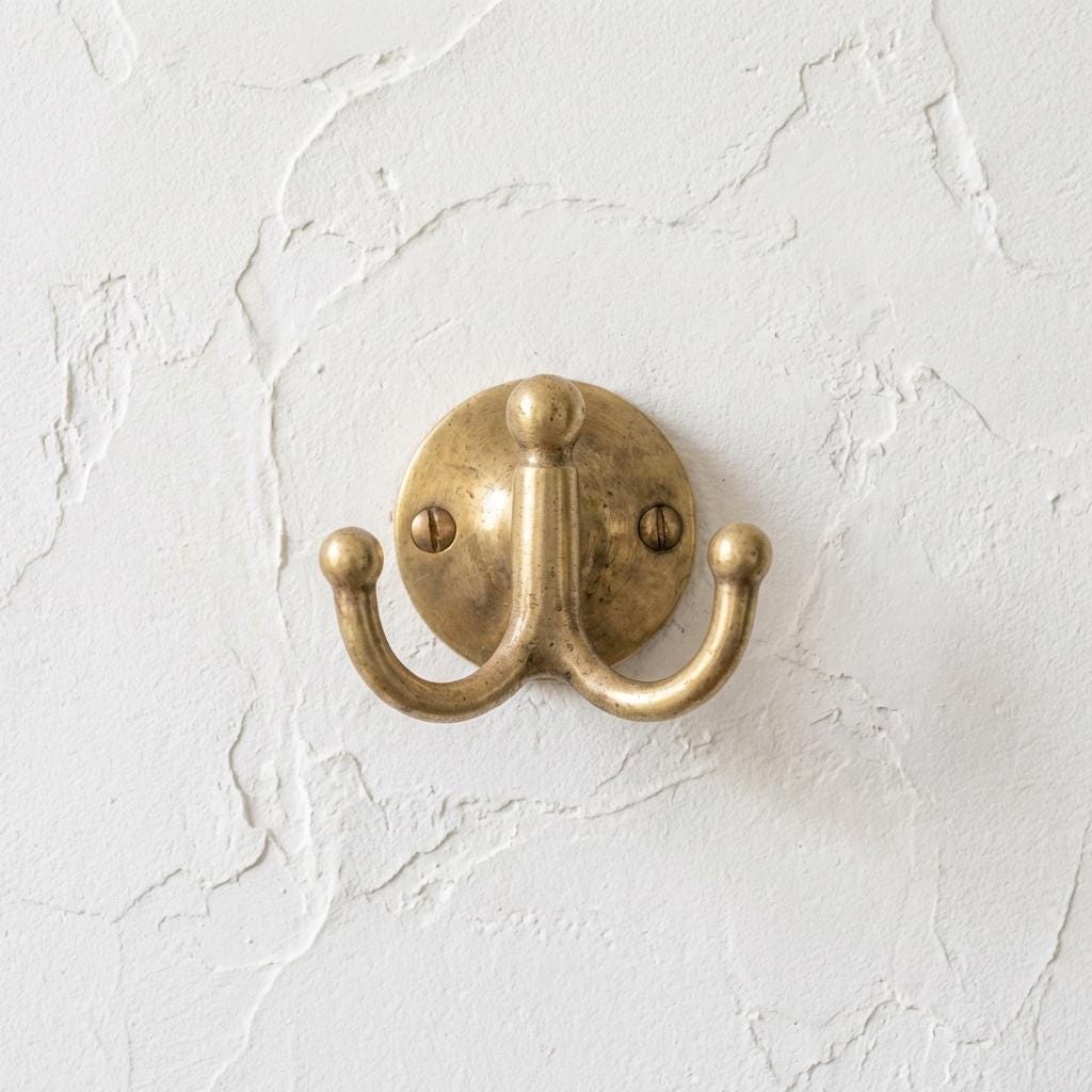 Unlacquered brass double wall hook mounted on a textured wall.