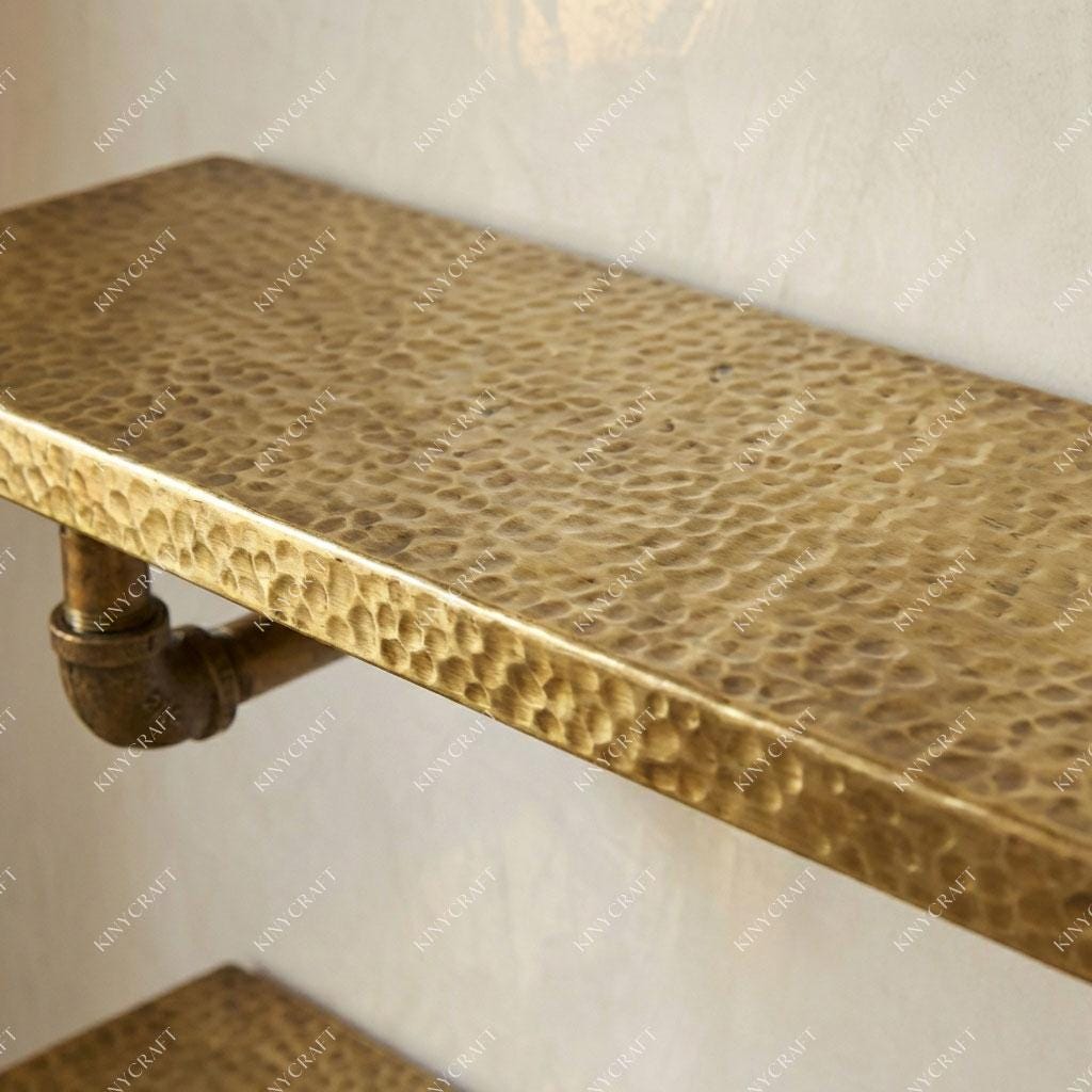 Wall-mounted hammered brass shelf with pipe supports for elegant open storage and display.