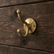 Handmade solid brass double wall hook mounted on a rustic wooden wall.