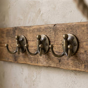 Handmade antique brass double wall hook mounted on a textured plaster wall.