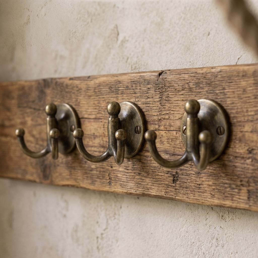 Handmade antique brass double wall hook mounted on a textured plaster wall.