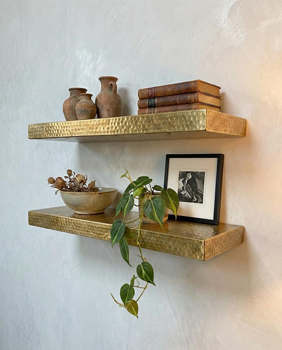 Hammered brass floating wall shelves displaying books, ceramics, and decorative accessories.