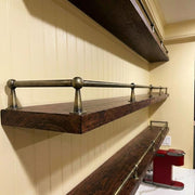 Antique brass shelf rail mounted on dark wood floating shelves for kitchen storage.