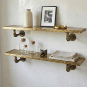 Handmade hammered brass floating wall shelf with pipe brackets mounted on a plaster wall.