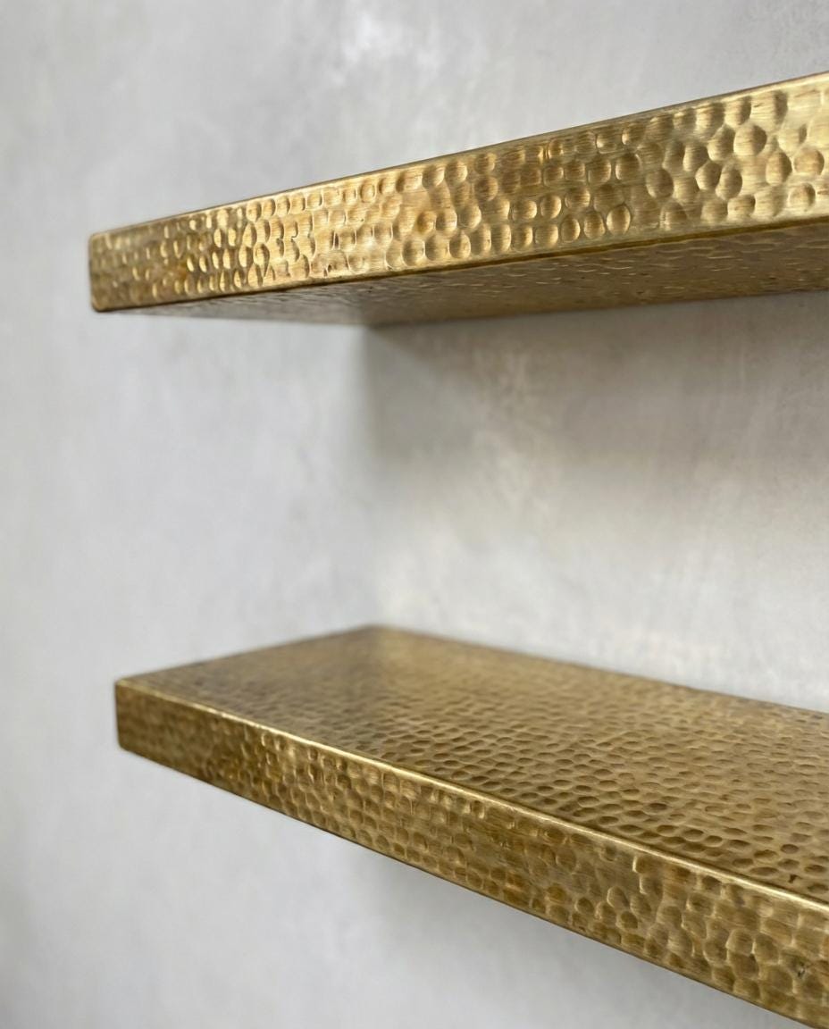 Luxury floating brass shelf installed on a textured plaster wall with decorative styling.