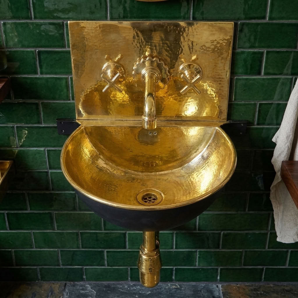 Front view of polished brass wall hung sink with black bowl, brass bottle trap and green tiles