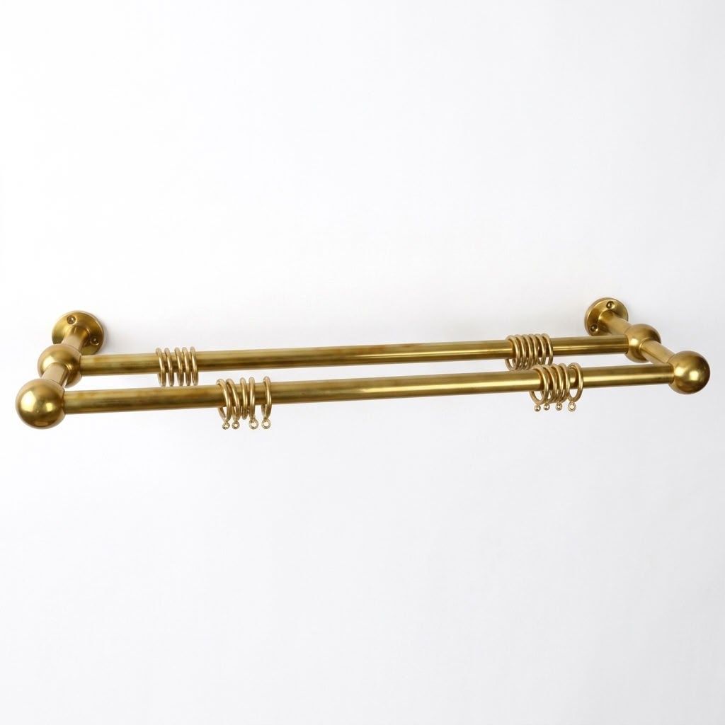 Unlacquered solid brass double curtain rod with ball finials, wall brackets and eyelet rings on a white background